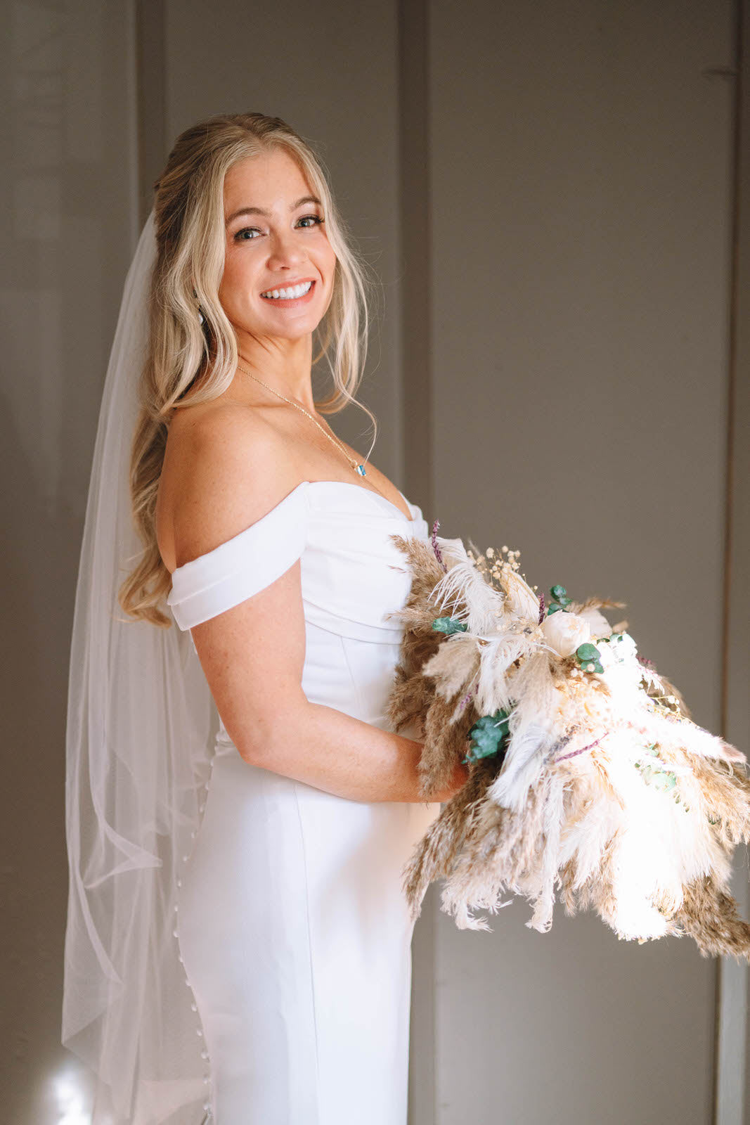 Bride in a fingertip cut edge wedding veil and form fitting wedding dress holding a bouquet with pops of turquoise