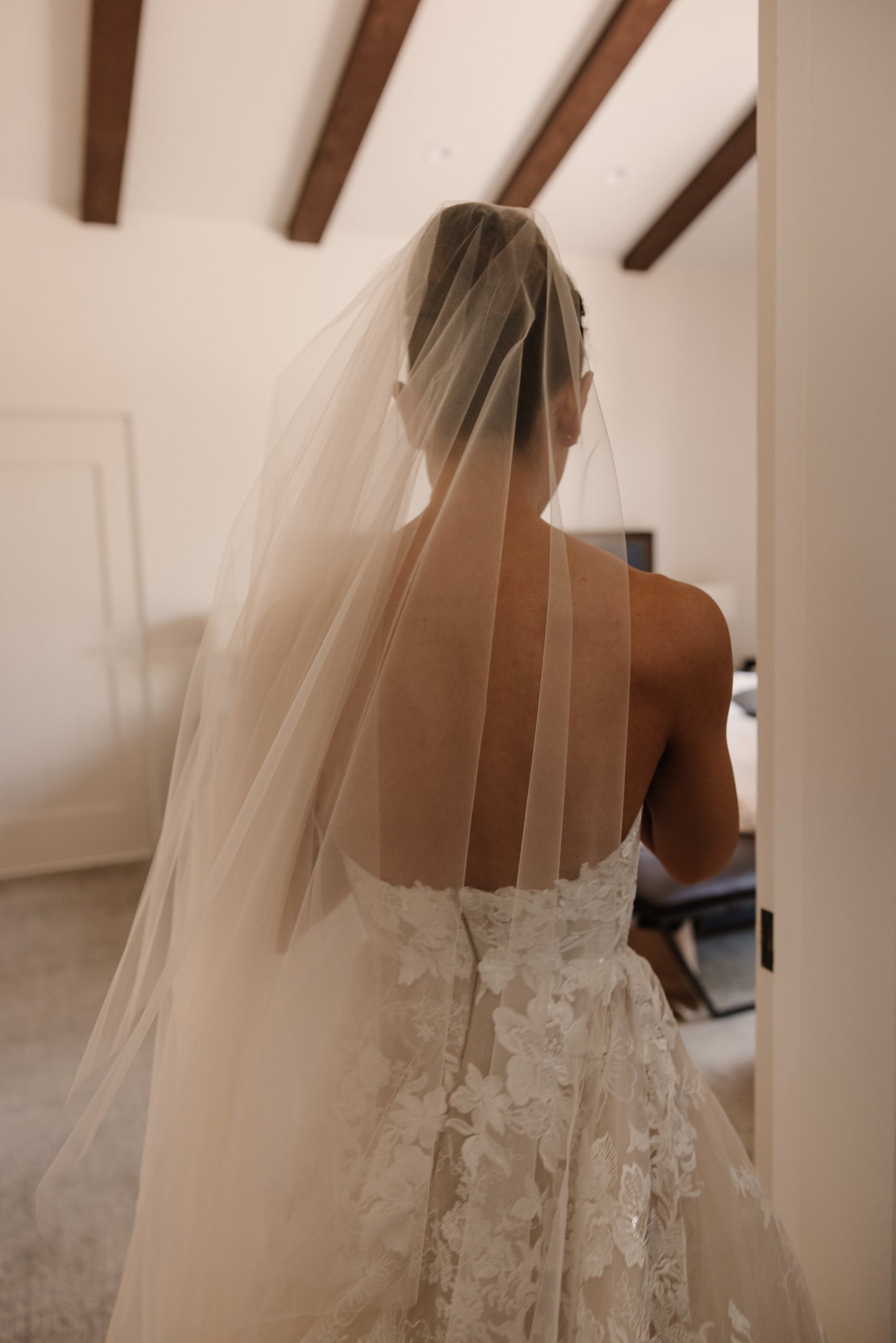 Bride wearing a lace wedding dress and long blusher cathedral drop laceindoors.