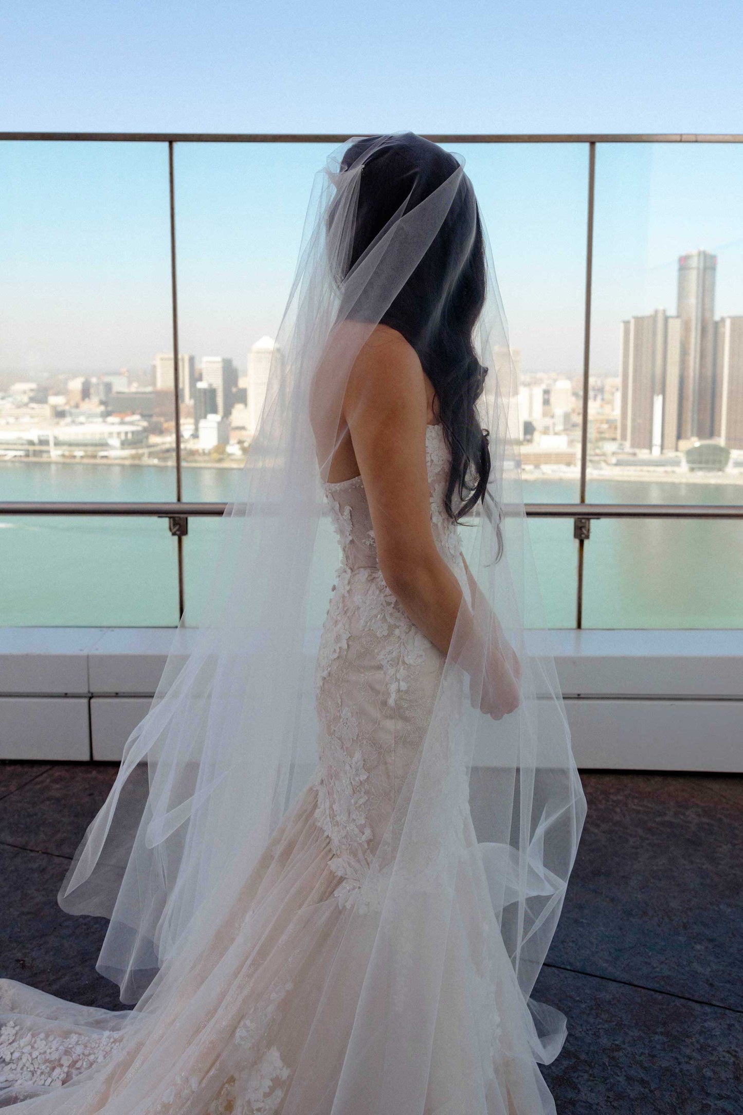 DIY Bride in a blush wedding dress with a long veil standing on a rooftop with city skyline in the background