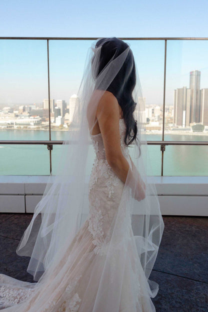 DIY Bride in a blush wedding dress with a long veil standing on a rooftop with city skyline in the background