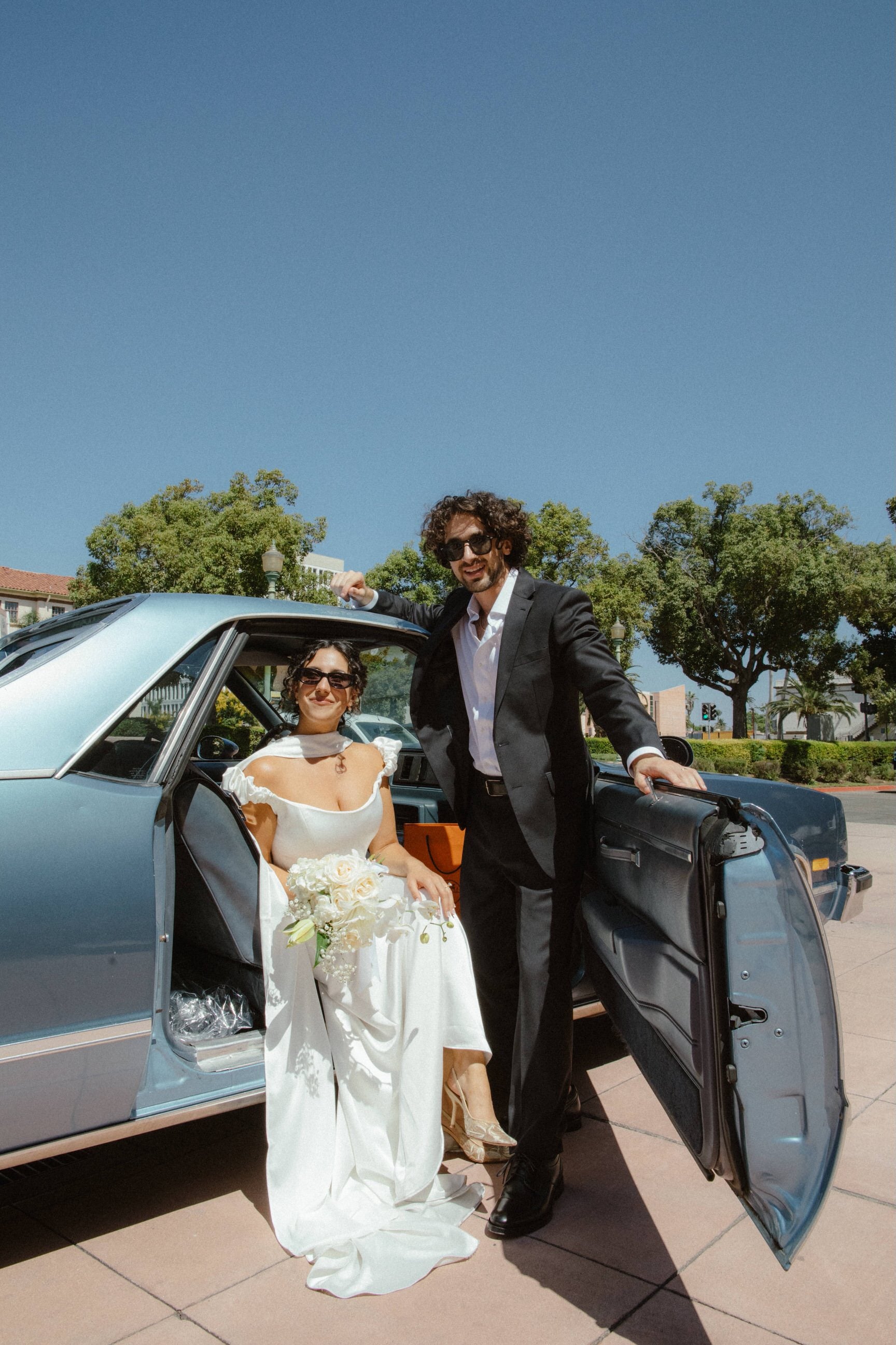 off the shoulder corset bridal gown with silk satin narrow neck scarf on bride sitting in getaway car