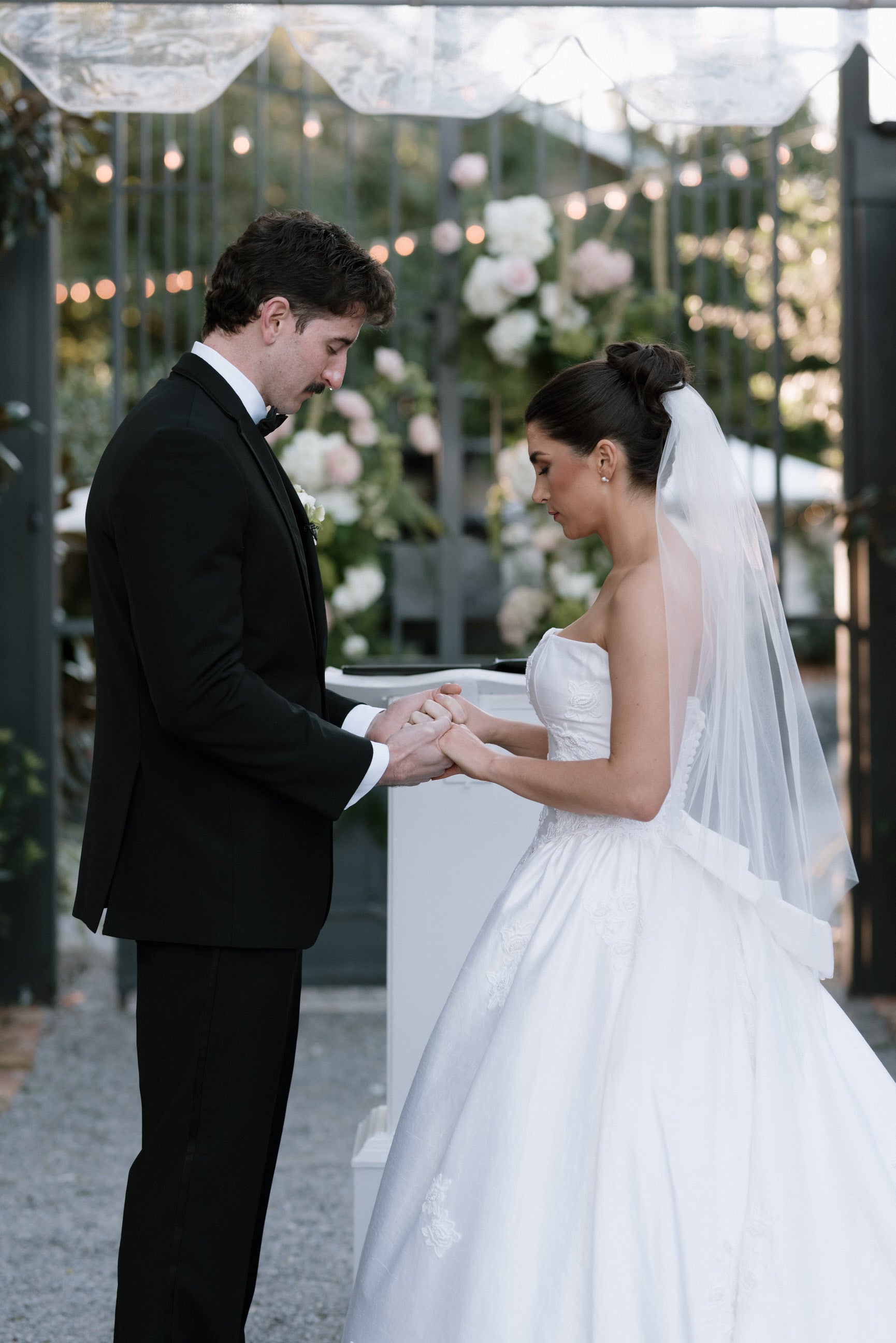 strapless ballgown satin gown with fingertip white raw edge veil under high curled updo as bride stands at alter
