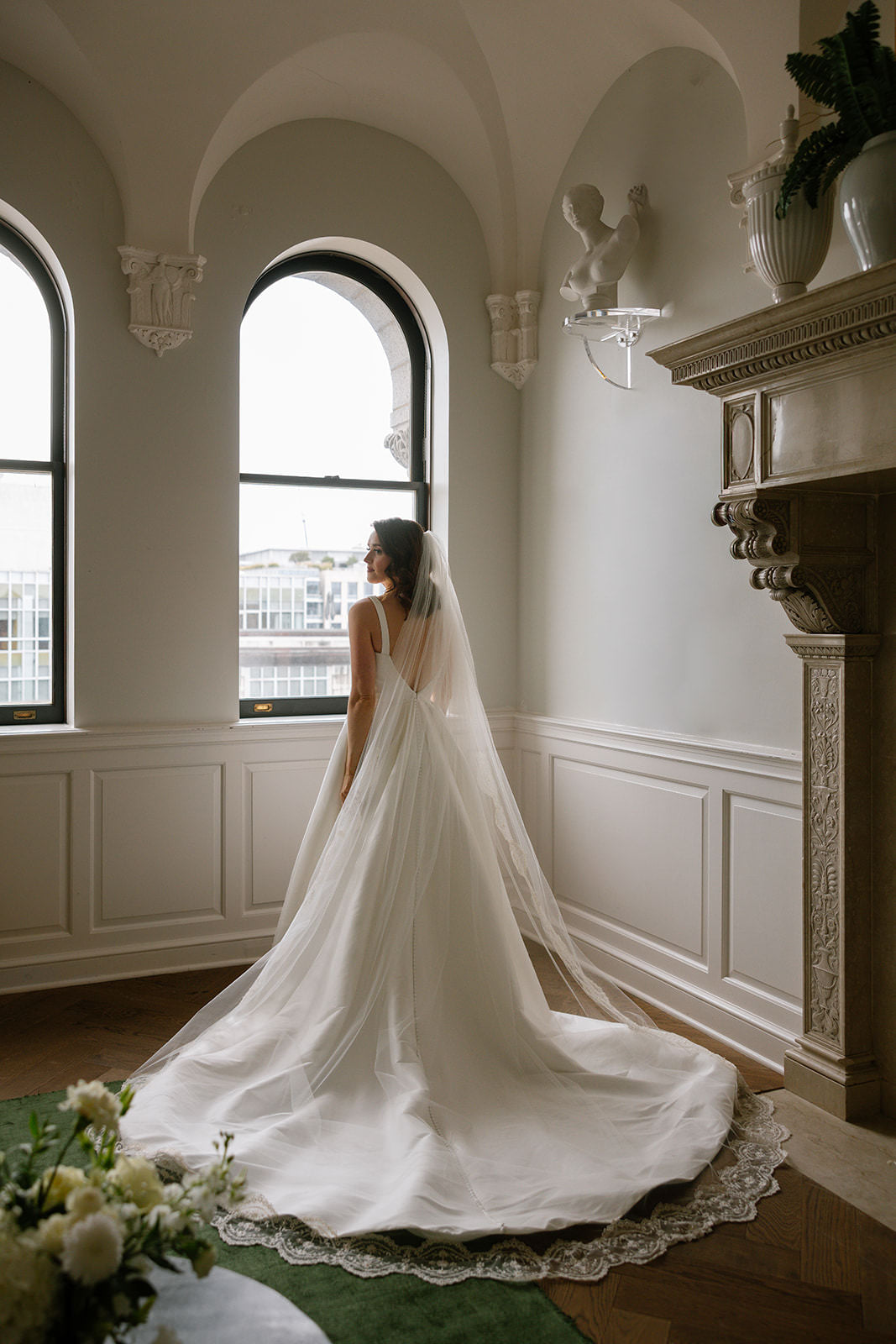 Woman in a white classic A line wedding dress with a long redesigned wedding veil with lace and pearls with arched windows and decorative elements.