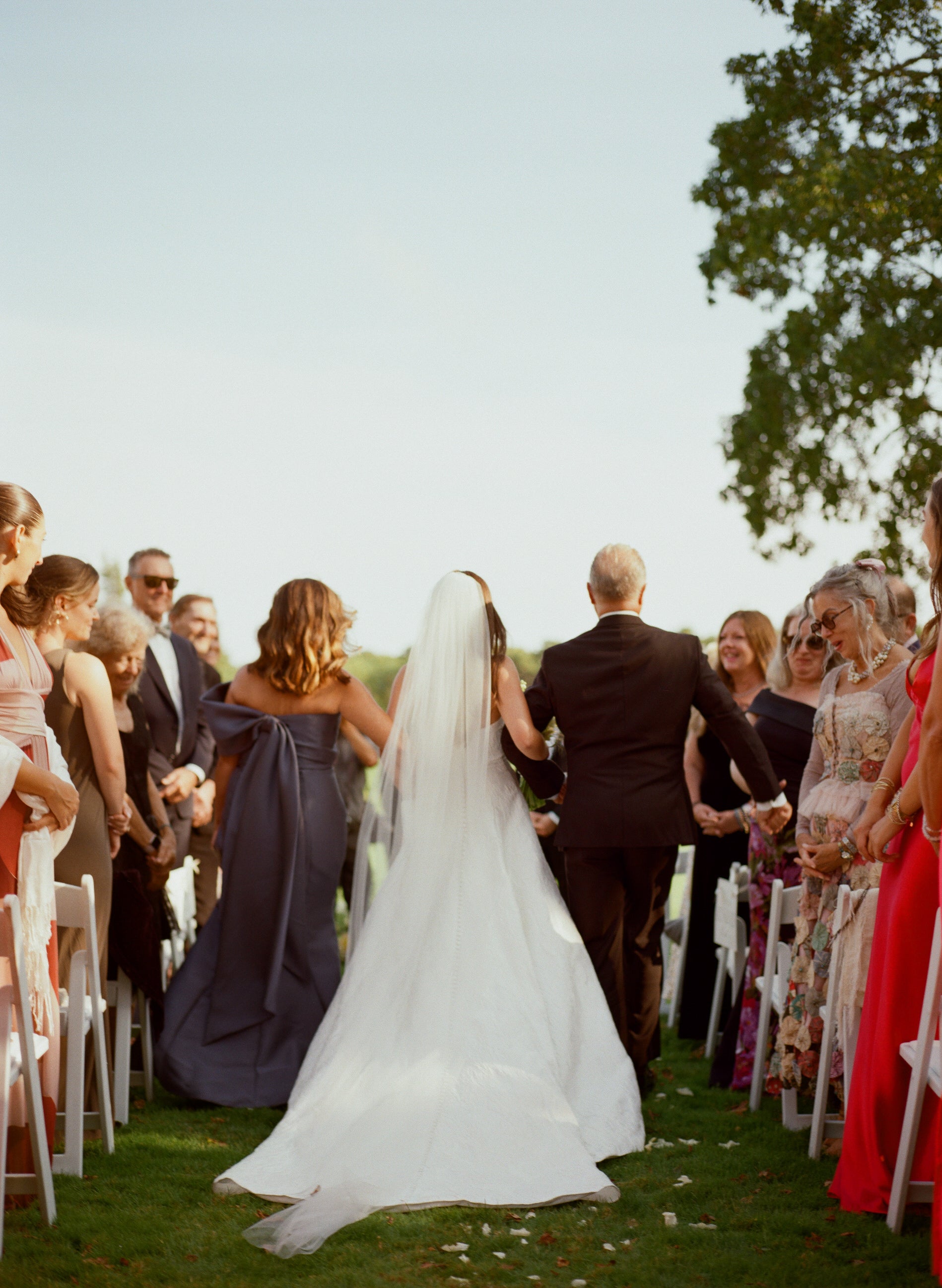 Wedding ceremony with a bride walking down the aisle in simple ivory raw edge cathedral veil, surrounded by guests.