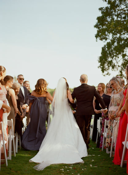 Wedding ceremony with a bride walking down the aisle in simple ivory raw edge cathedral veil, surrounded by guests.