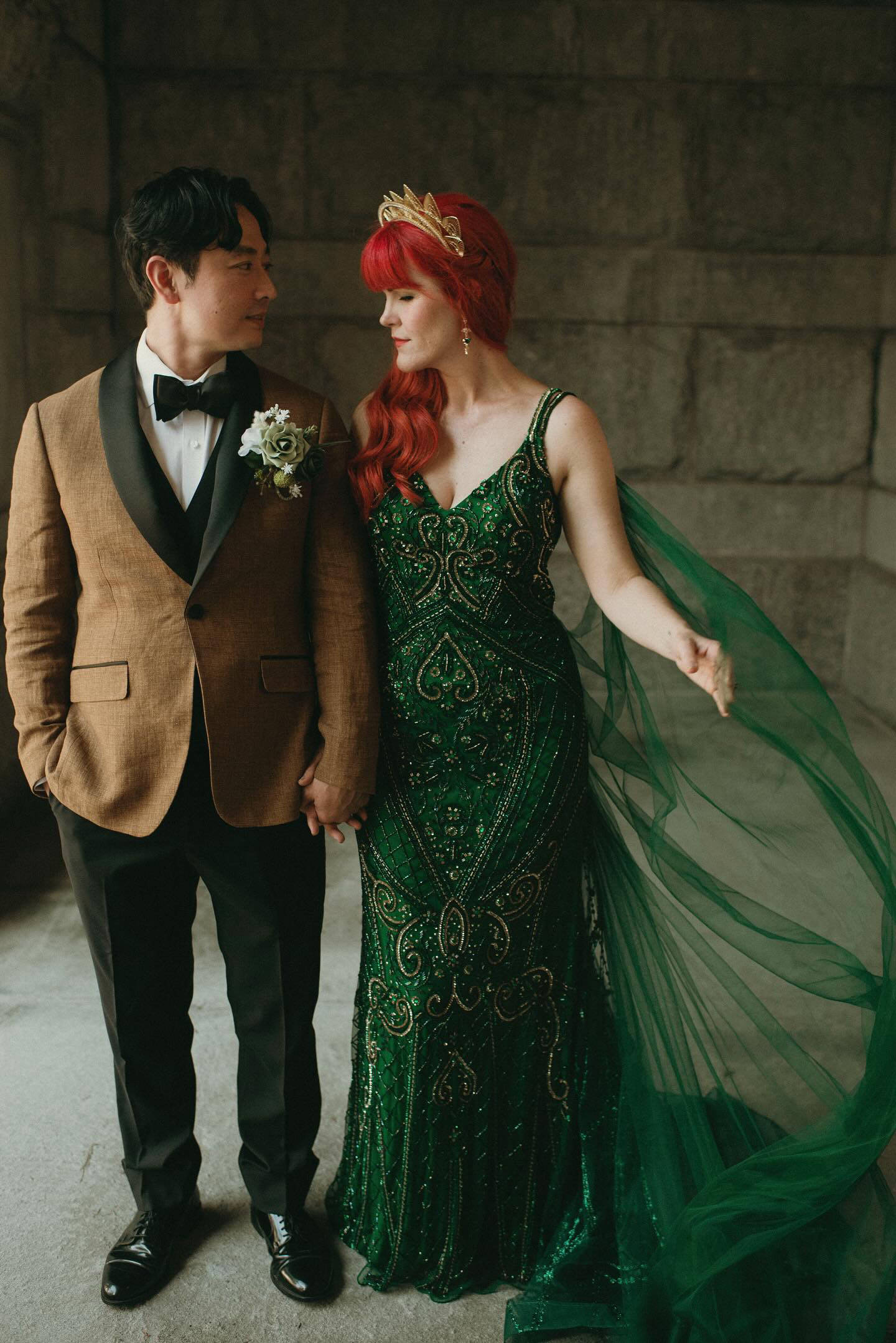 Bride and groom holding hands, redhead bride in a green dress with a long tulle  cape veil that she sewed herself