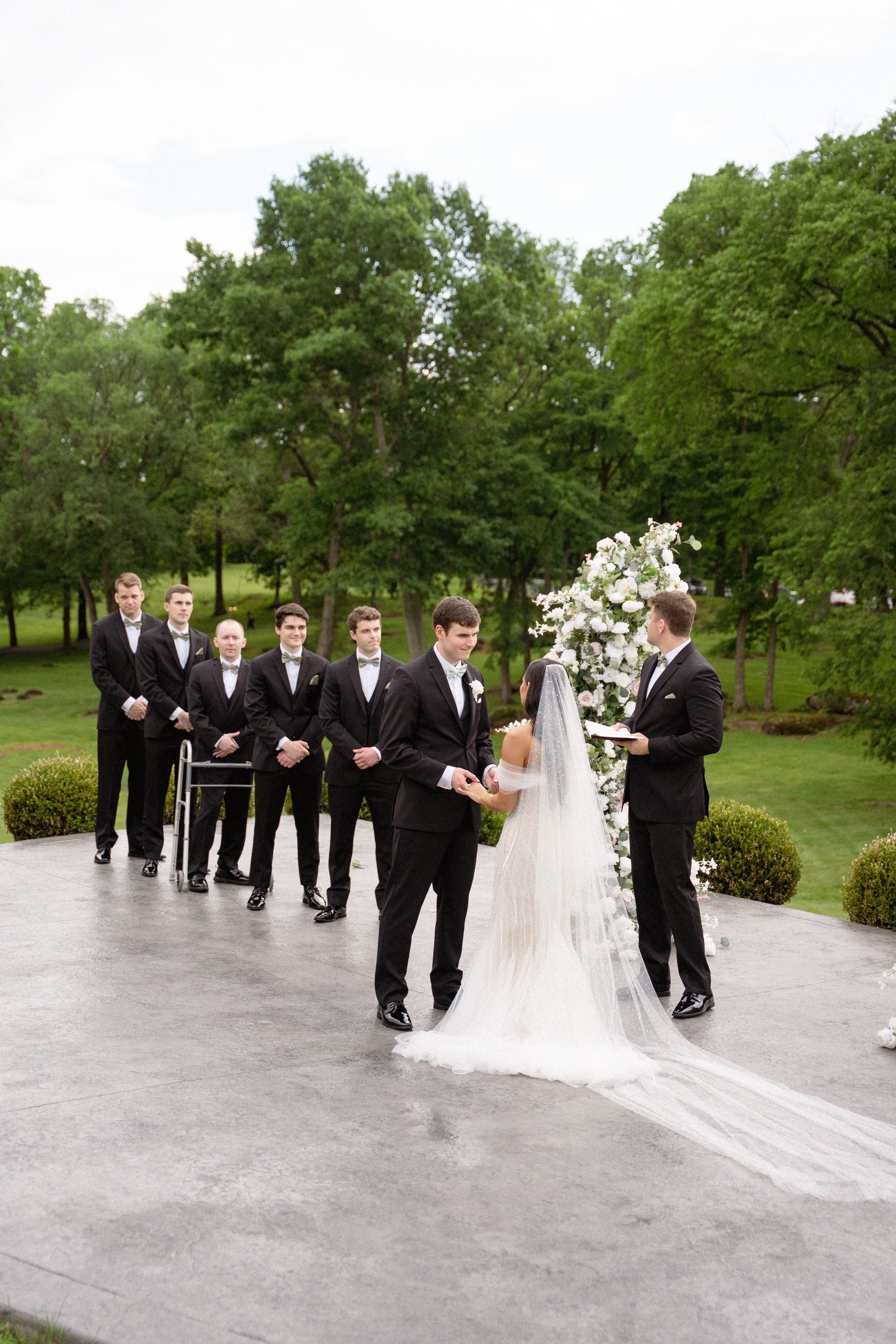 Wedding ceremony with a bride in royal length sparkly veil and groom in a park setting 