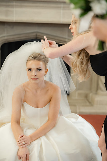 Bride sitting  adjusting puffy and four layer veil in an indoor setting