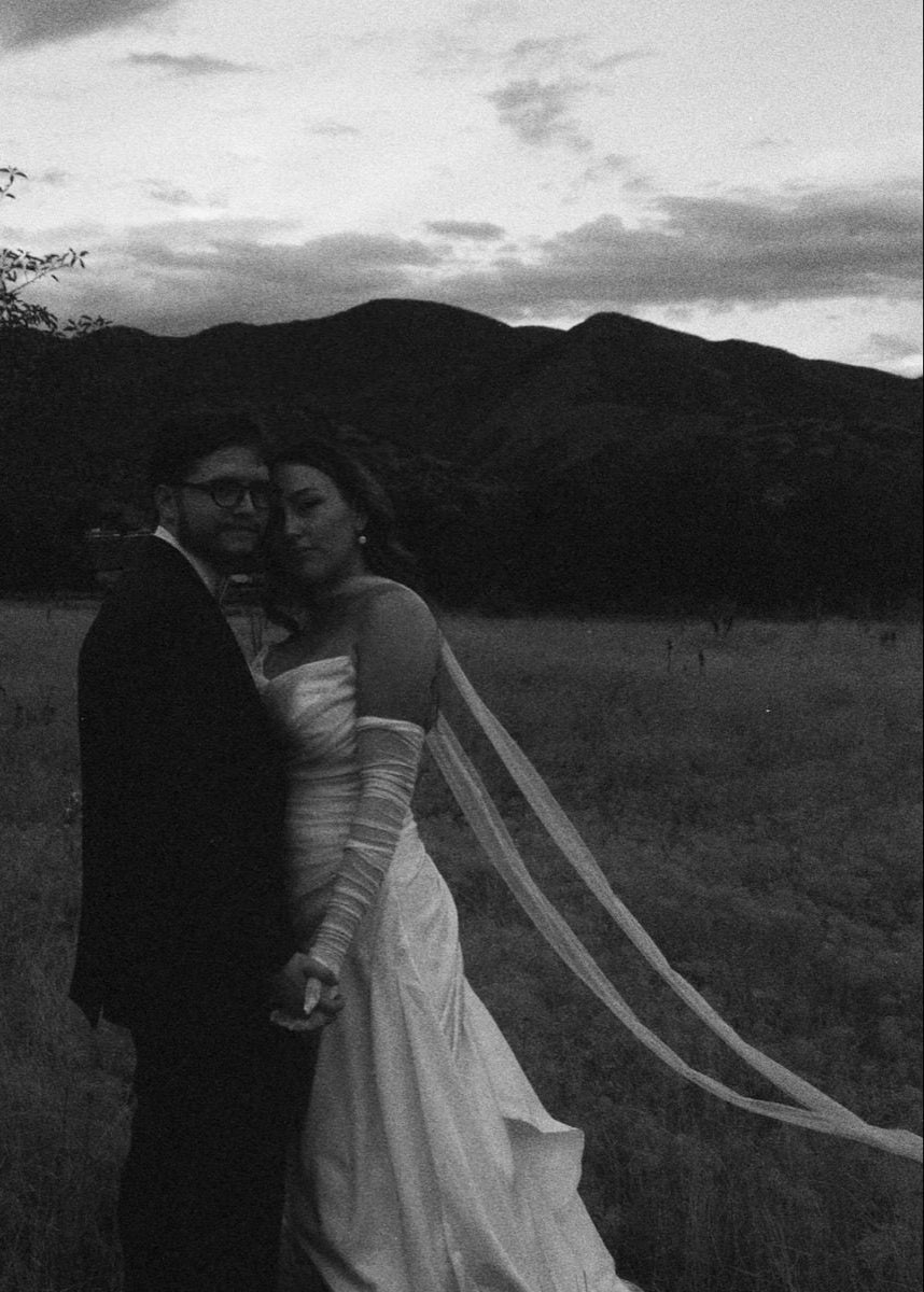Black and white photo of a couple in wedding attire with bride in extra skinny long bridal scarf and tulle gloves