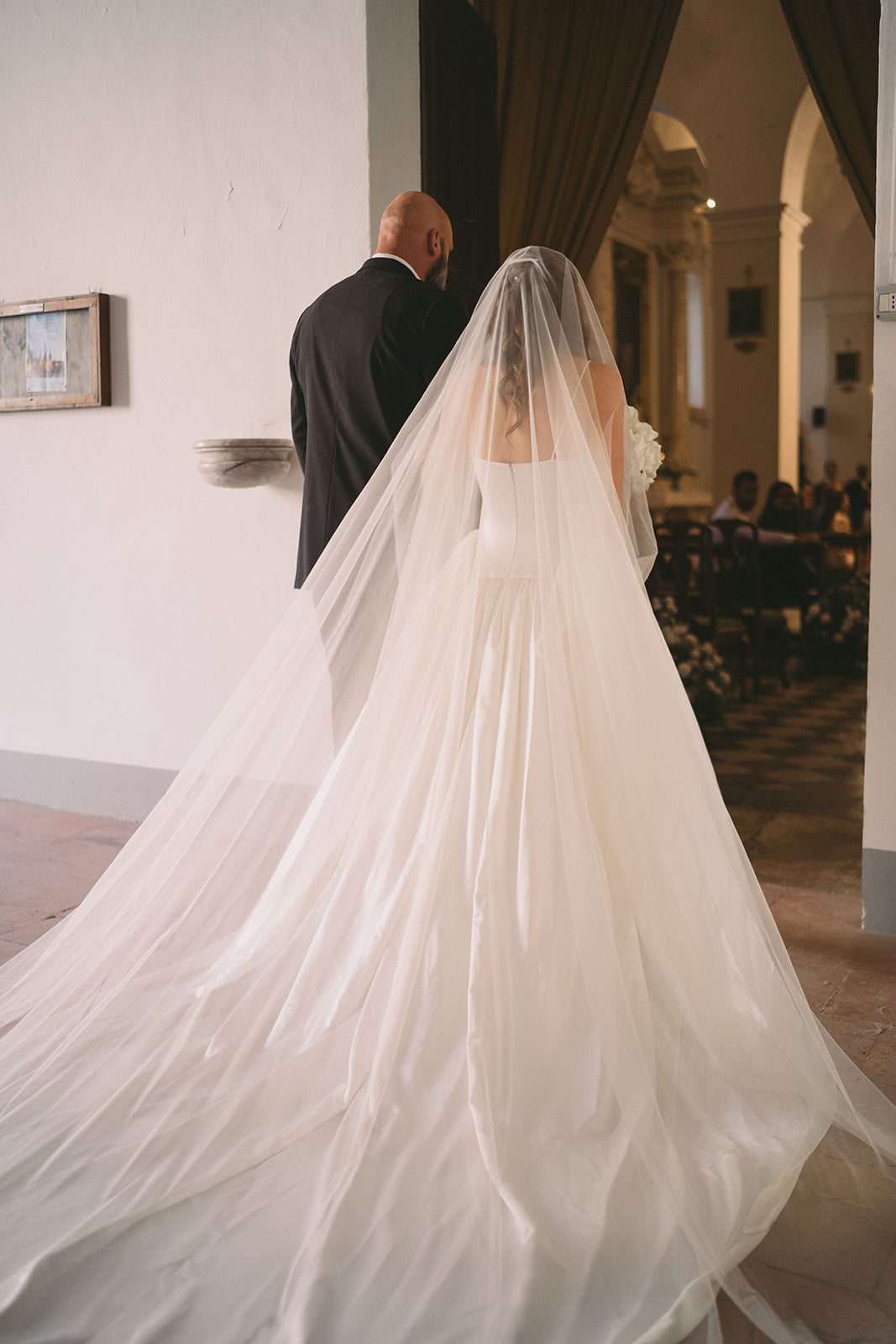 custom extra wide royal length wedding veil in light ivory soft tulle on bride entering church 