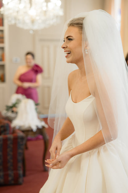 Bride in a white wedding dress with a puffy veil, smiling indoors in cat eye bridal gown dress