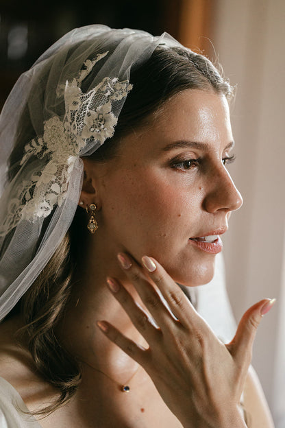 bride wearing a lace Juliet cap veil and earrings, with blush manicured nails