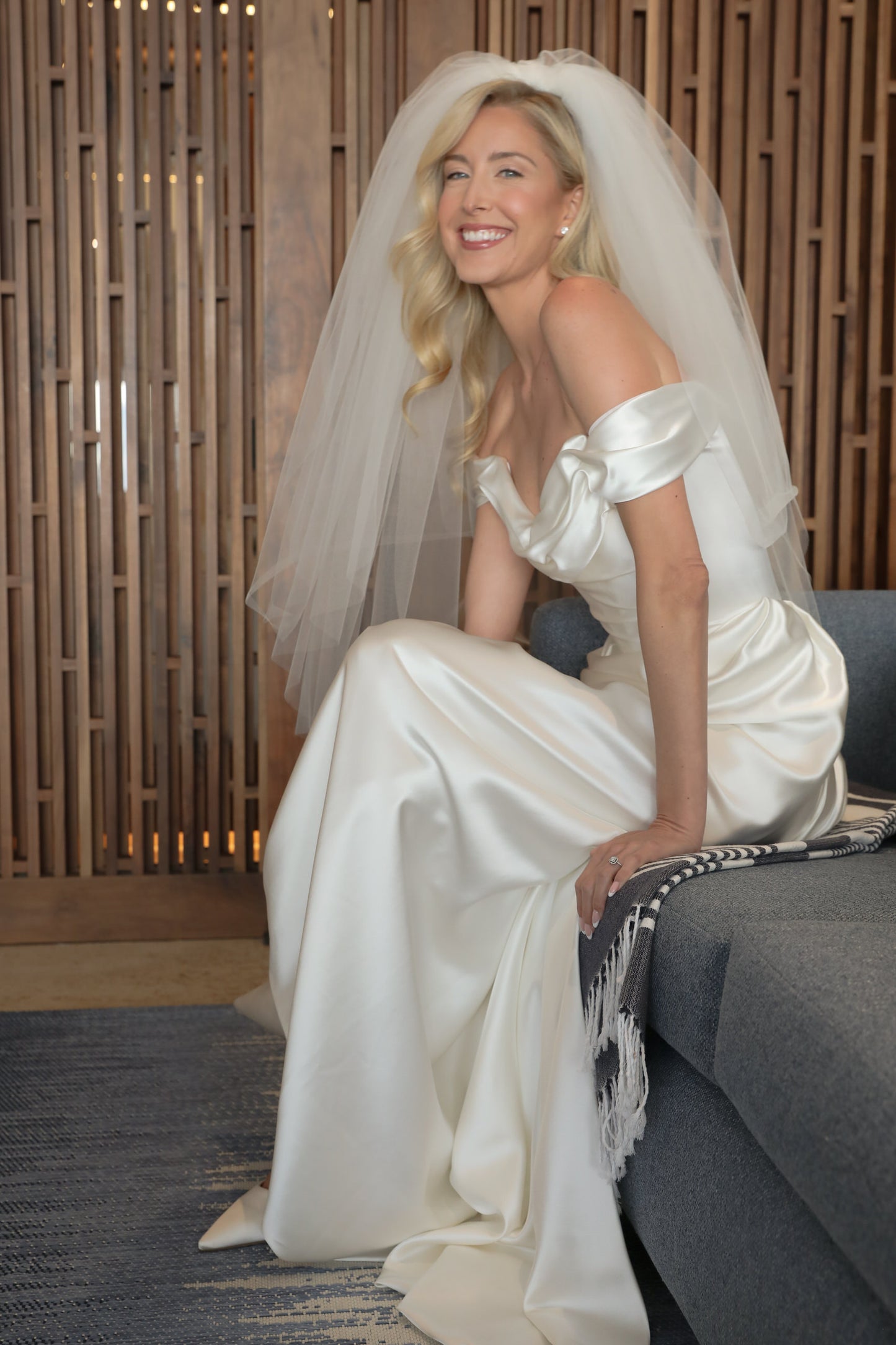 bride in a white Vivienne Westwood  wedding dress with a puffy two layer veil sitting on a couch.