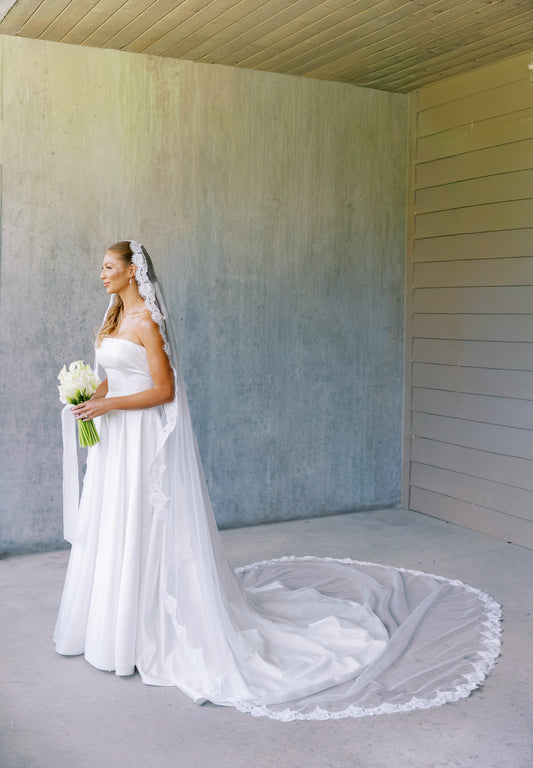 Bride in a strapless off white A line wedding dress with a long train wearing royal length eyelash lace mantilla wedding veil