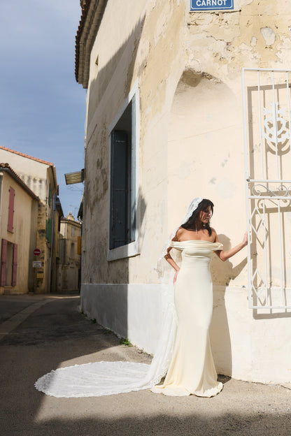 Woman in an ivory off shoulder wedding dress standing on Italian  street with a long lace cathedral bridal veil