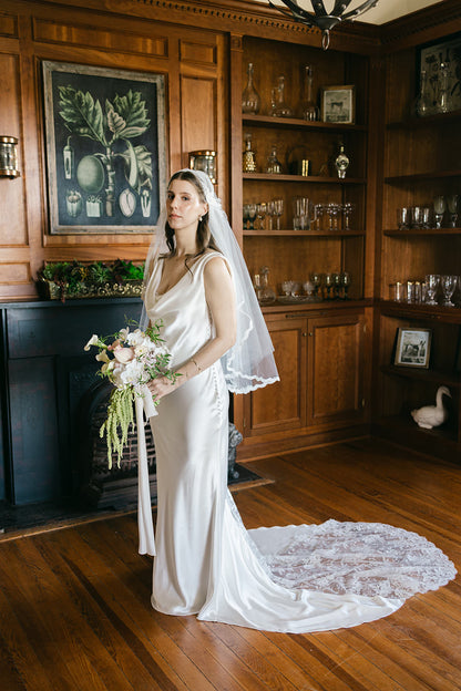 bride wearing a white draped-neck bridal gown and a Juliet cap veil with fine scallop edging that is mid length 
